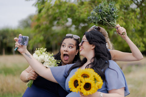 Candid moment of a wedding guest in a blue dress taking a selfie with a sunflower bouquet.
