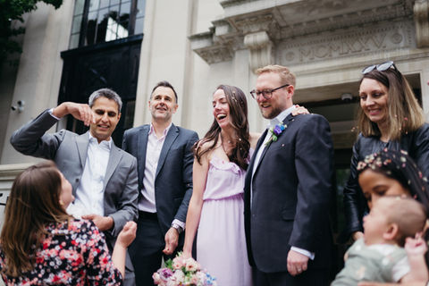 Group of wedding guests sharing a celebratory laugh outside a traditional town hall venue in London.