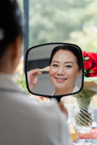 Creative bridal prep photography showing the bride's reflection in a hand mirror while applying makeup.