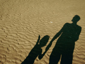 Long shadows on sand show an adult holding hands with a child