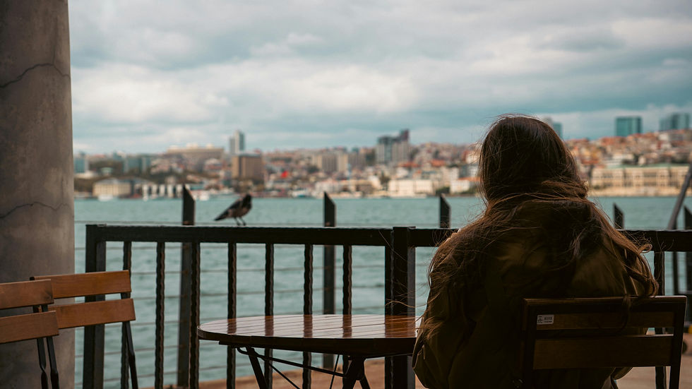 Woman sitting alone at a waterfront table, lost in thought on a cloudy day