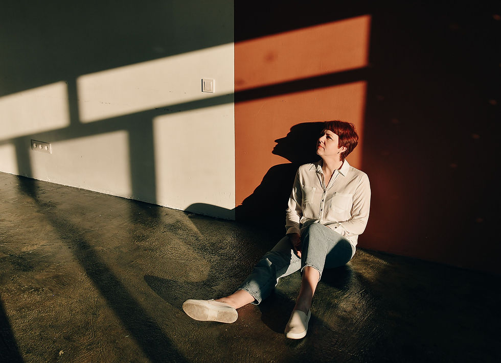 Woman sitting alone on the floor in light and shadow, quietly reflecting on carried emotional weight
