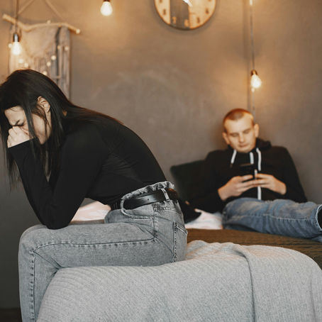 Woman sitting alone in distress while partner is disengaged in the background, showing emotional distance in a relationship