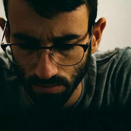 Man with glasses looking down, weighed down by guilt and the habit of constant apologizing