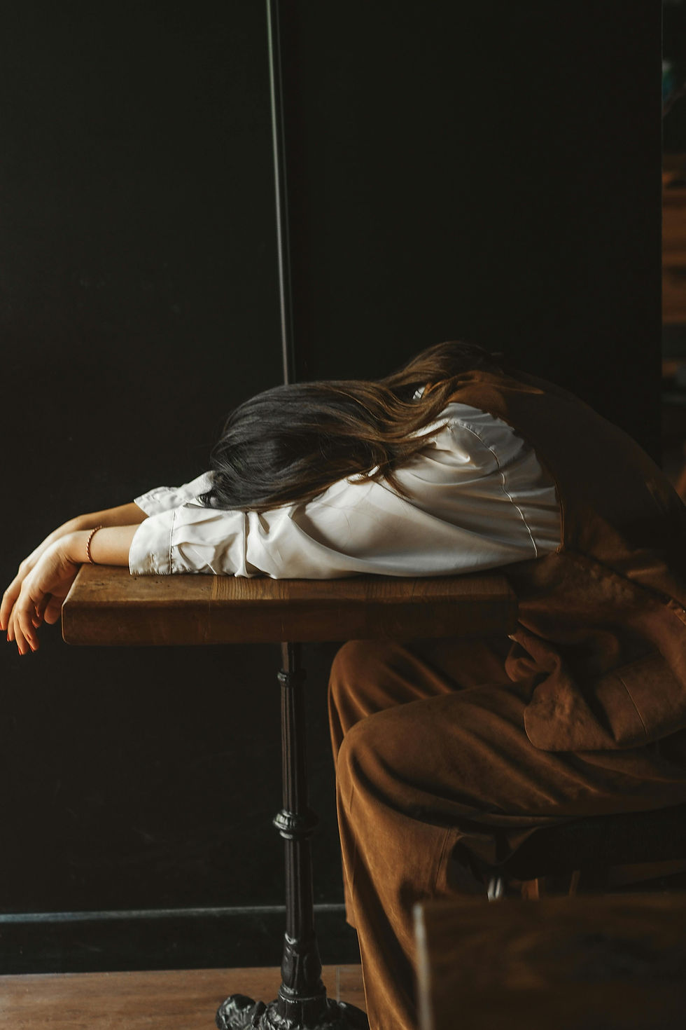 Woman with head down on a table, overwhelmed and exhausted from constant self-criticism