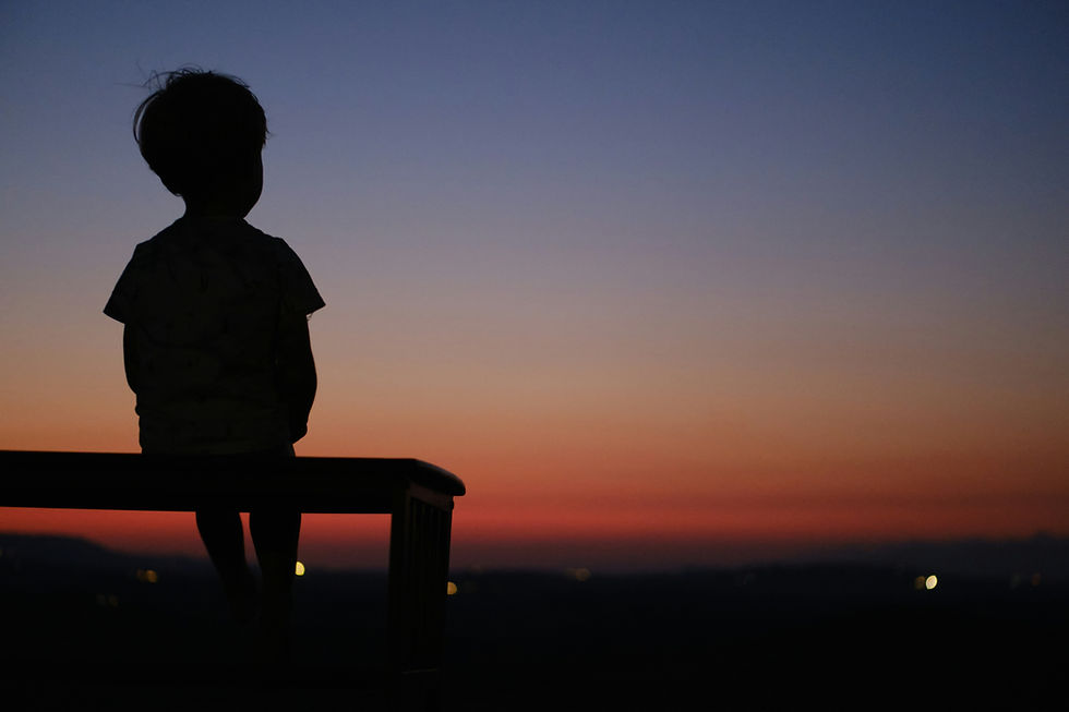 Young child sitting alone on a bench in the dark, looking away