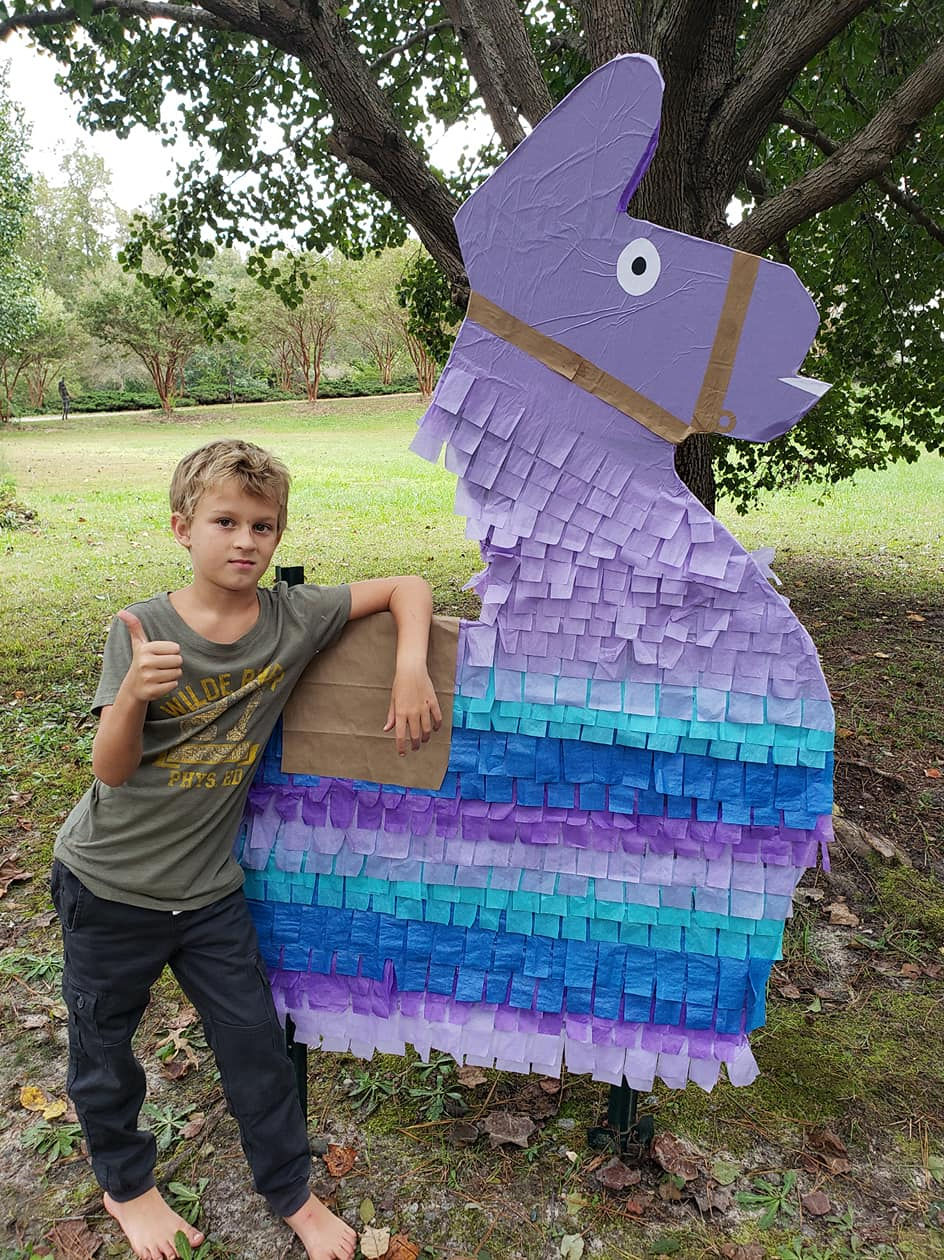 child standing next a huge fortnite llama decoration