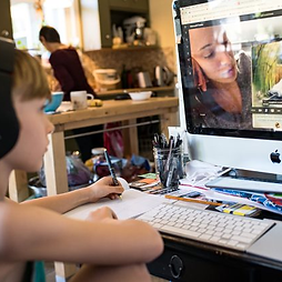 Young boy wearing headphones participating in an online learning session, writing notes while watching a lesson on a computer