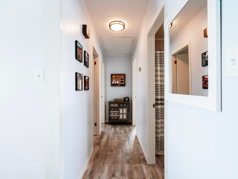 Light blue hallway with framed pictures and a dresser, leading to a bathroom with a shower curtain,  and a mirror on the wall