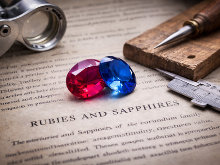 Ruby and sapphire gemstones on a jeweller’s workbench with loupe, caliper, and wooden bench pin, representing artisan craftsmanship and gemstone evaluation