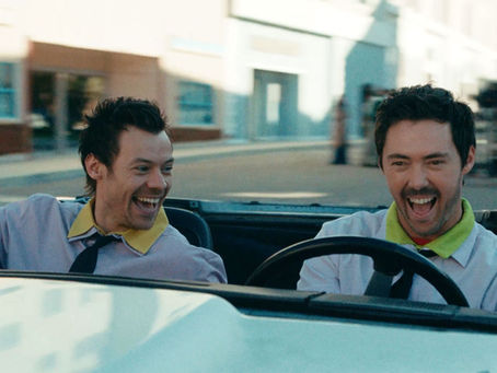 Dois homens sorrindo em um carro conversível durante cena em Nova York, em imagem ligada ao universo de Harry Styles.
