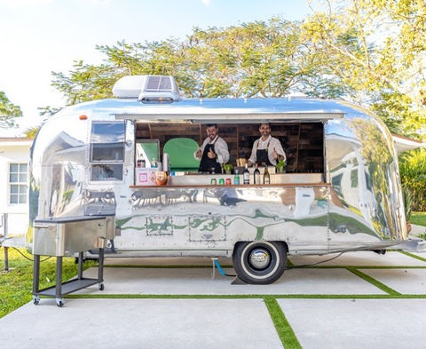 Two STARBAR Miami bartenders smiling and expertly crafting cocktails behind a vintage Airstream mobile bar.