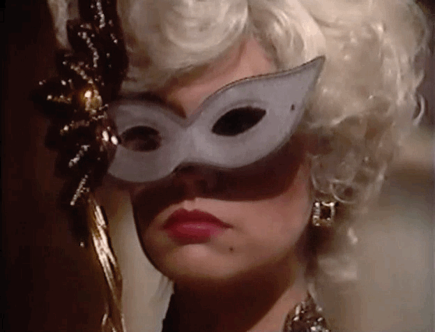 Anna Devane in 80s wearing a Halloween costume and taking off a mask