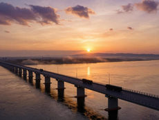 Tumen River road bridge between North Korea and Russia at golden hour, aerial view showing new multi-lane crossing alongside the rail bridge, military truck convoy in silhouette, dramatic sunset, September 2026 opening — CES Intelligence North Korea 2026 geopolitical risk assessment