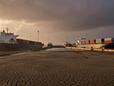 Cracked dry lakebed of Gatun Lake in front of the Miraflores locks, container ships queuing on the Panama Canal at dusk — illustrating Latin America's El Niño 2026 drought and supply chain exposure.