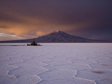 Salar de Uyuni at dusk with distant Andean volcano and a small lithium extraction facility, illustrating the Bolivia 2026 geopolitical risk assessment