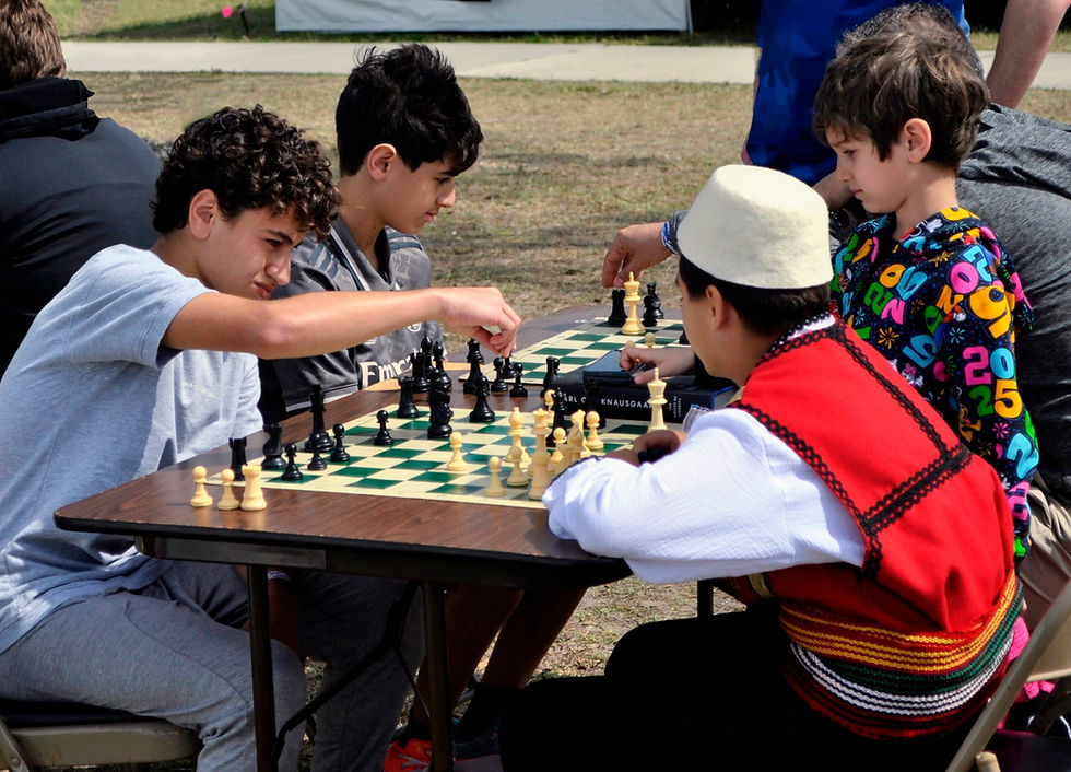 4 boys play chess, one is a cultural costume.