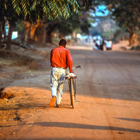 local walking next to a bicycle on a dirt road