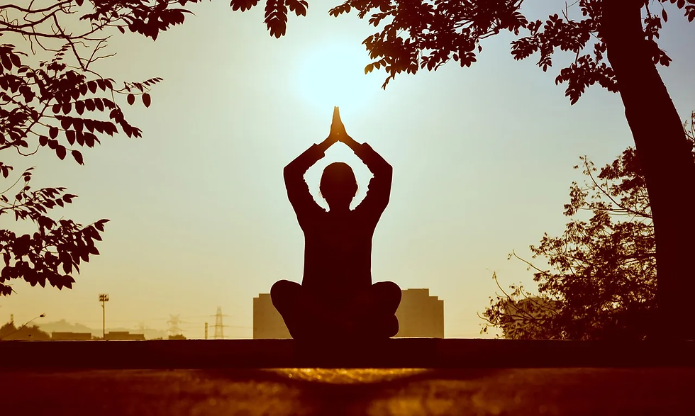 Silhouette of a person meditating with raised hands at sunrise. Trees frame the scene, with a calm, peaceful mood.