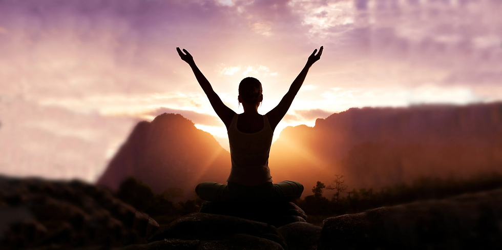 Silhouette of a person raising arms, sitting cross-legged on rocks at sunrise. Background shows mountains and a purple-orange sky. Calm mood.