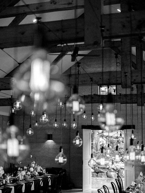 Photo en noir et blanc représentant l'organisation d'événements stylisés, avec une guirlande d'ampoules suspendue au plafond et une salle décorée, créant une atmosphère intime et moderne.