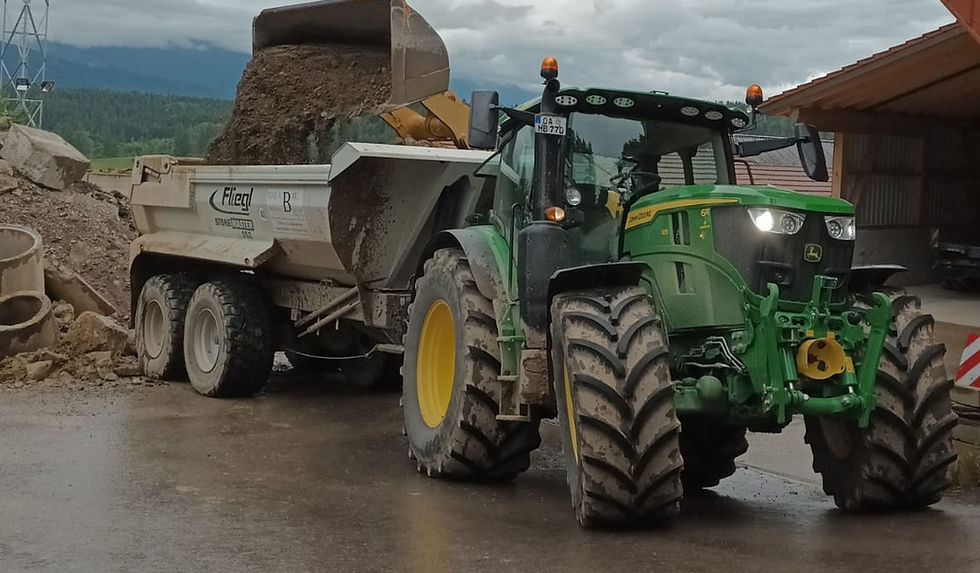 Grüner Traktor mit beladenem Anhänger auf einem Betriebshof