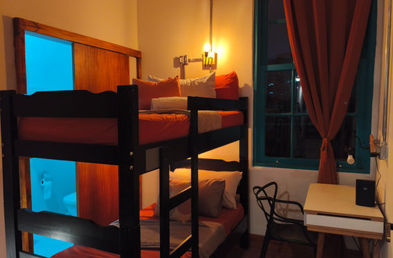 Quarto privativo com beliche, roupa de cama laranja, escrivaninha e cortinas vermelhas