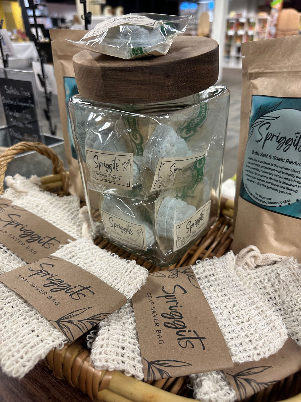 Spriggits display at AWD Studios showing a glass jar filled with foot shaped bath bombs and soap saver bags on the table