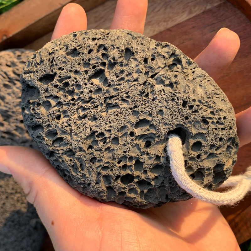 Hand holding a grey lava stone with a white rope, close-up view.