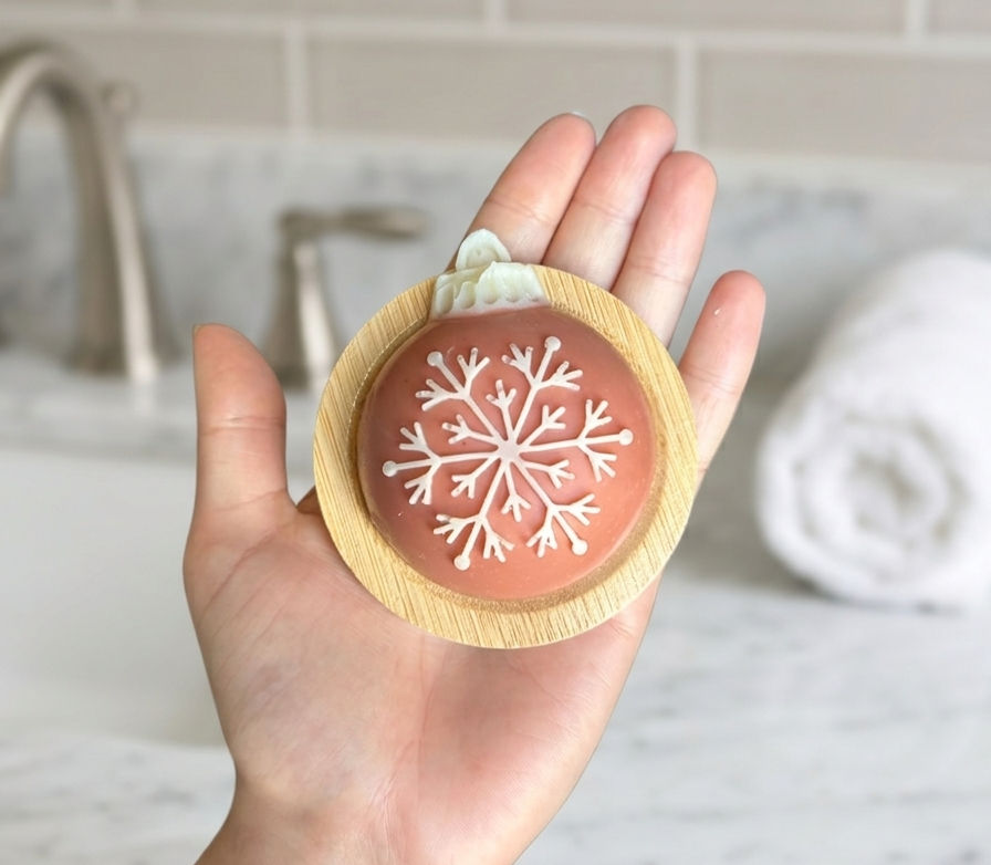hand holding a red ornament shaped soap featuring a white snowflake design on a soap dish