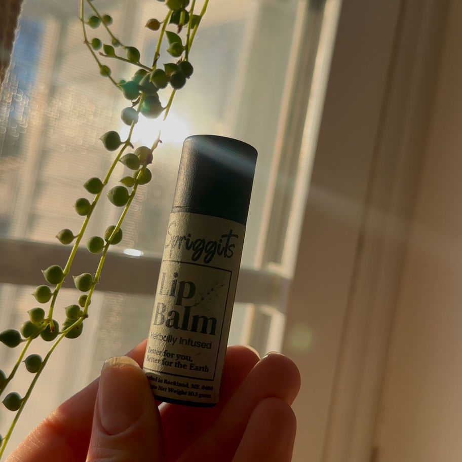 Spriggits lip balm in an eco-friendly cardboard tube being held in a hand against a sun beam background