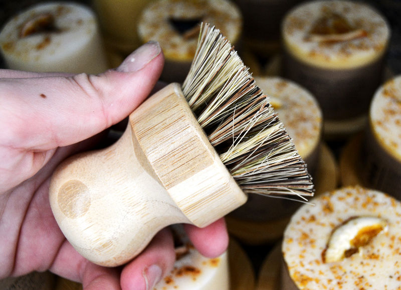 Hand holding scrubbing brush, the brush is made of wood and bristles