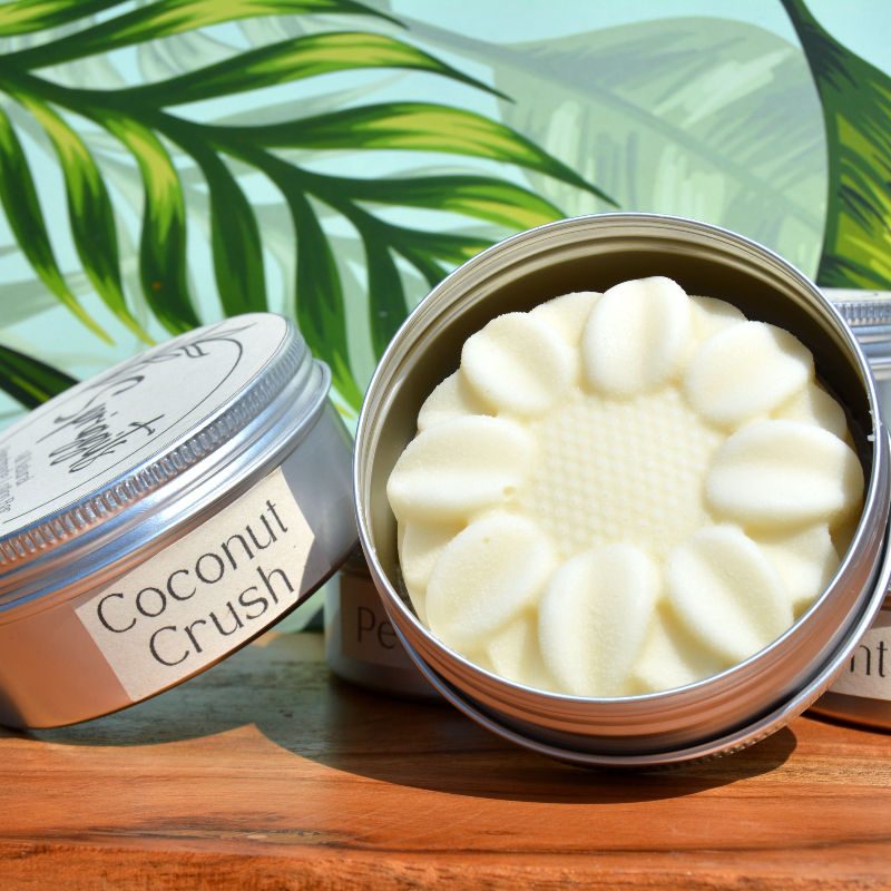 Coconut Crush lotion bar in a tin, tropical leaves background, close up.