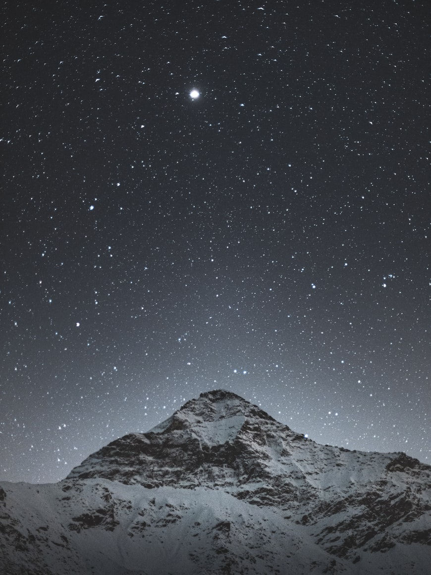 snowy mountain with galaxy and stars behind it