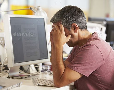 Stressed Man Working At Desk In Busy Cre