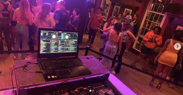 DJ laptop and turntables on the stage at Deer Park Tavern in Newark DE. People are mingling in the background 