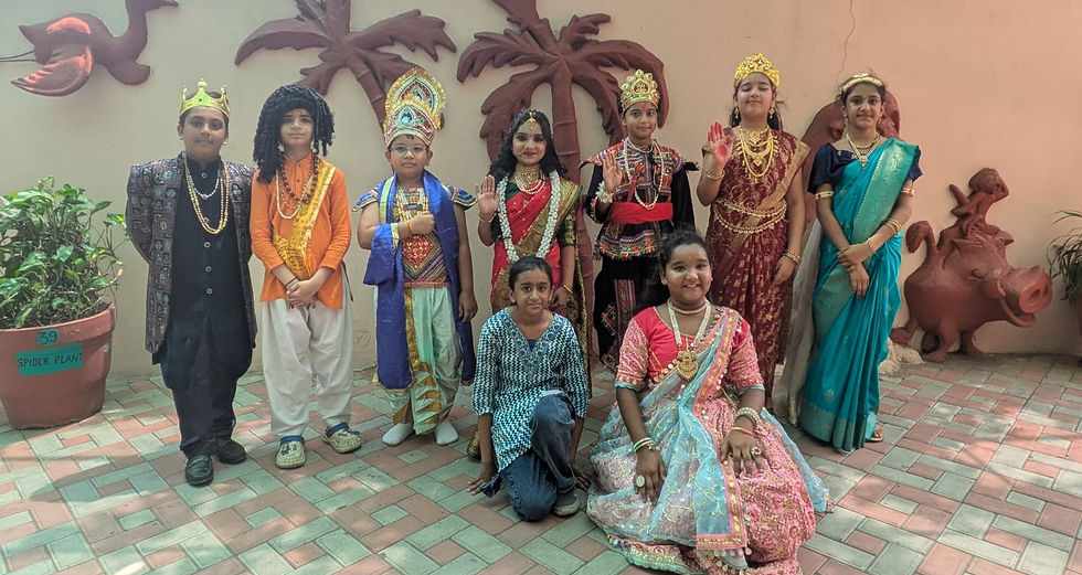 Group of children in royal and traditional costumes pose on a tiled courtyard with palm wall decor; a pot labeled Spider Plant.