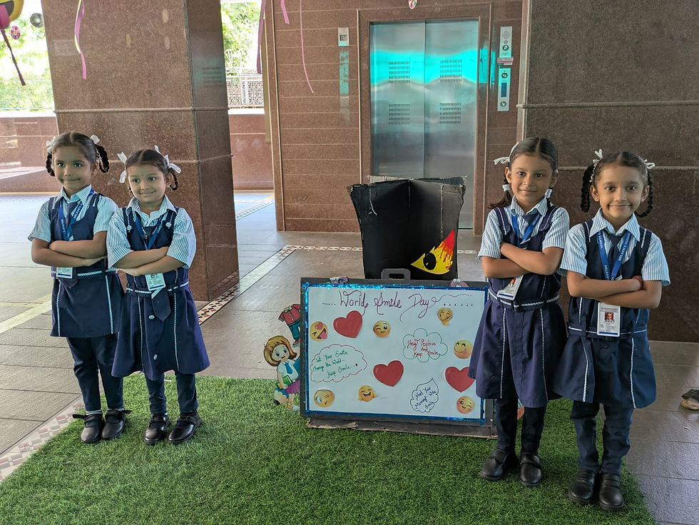 Four schoolgirls in navy uniforms stand by a World Smile Day poster in an elevator lobby, smiling.