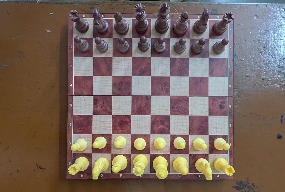 Top-down view of a wooden chessboard on a brown table, with brown and yellow pieces lined up for the start; A-H labels visible.