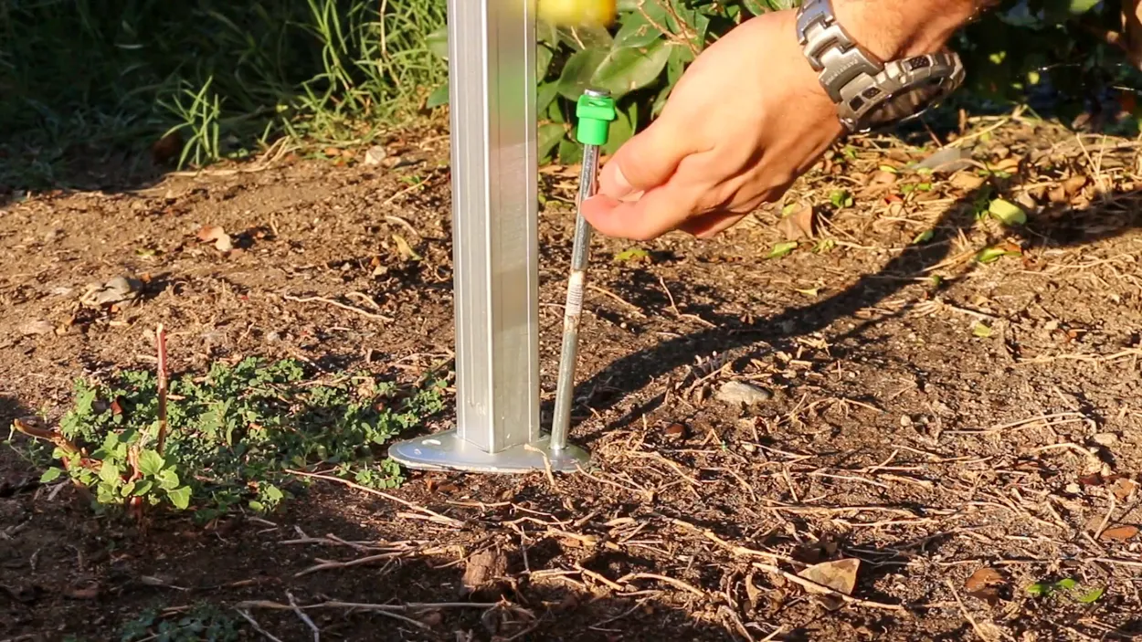 Hand driving a green-handled stake through a canopy leg base into the dirt