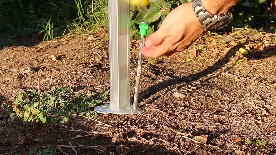 Hand driving a green-handled stake through a canopy leg base into the dirt
