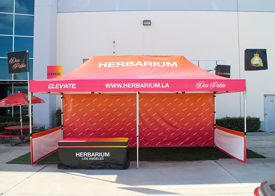 Custom 10x20 Herbarium canopy tent with printed graphics and attached advertising flags for outdoor promotions.