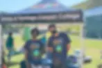 Two people in "EarthFest" shirts stand under a "Umoja at Santiago Canyon College" tent at a green campus event. One wears a mask.