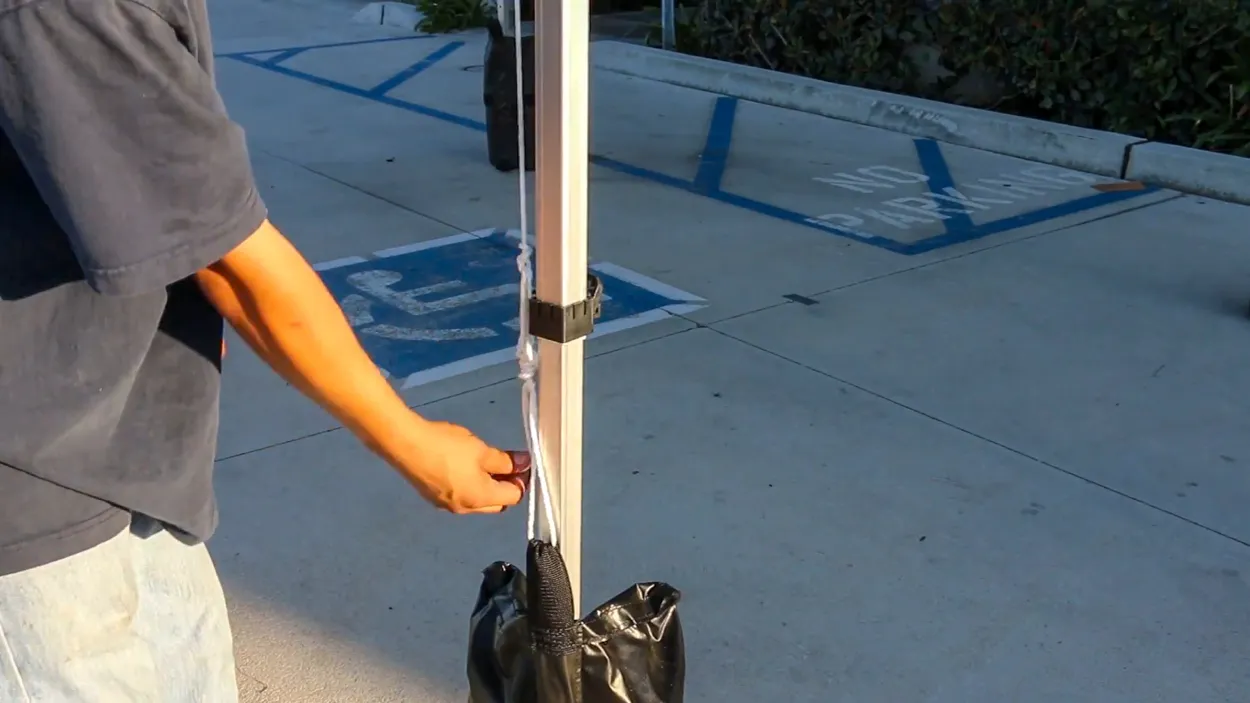 Rope fully tied and tightened around a canopy leg with weight bag in place