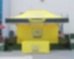 Yellow 10x15 tent canopy setup for "1 Day for Iowa" event. Bright backdrop and table cover display the same text.