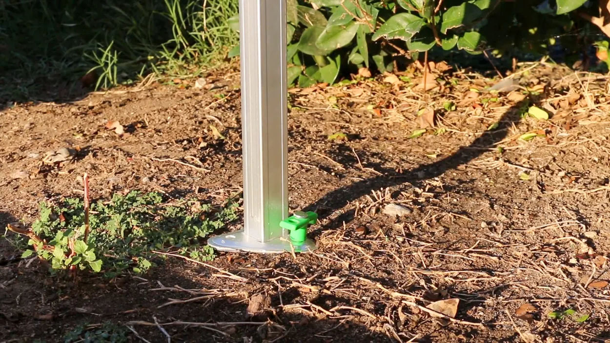 Canopy leg base secured in dirt with green-handled stake fully inserted