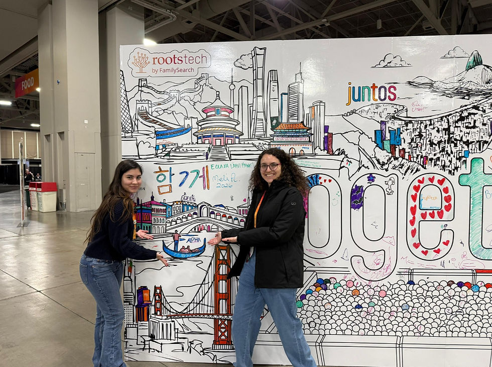 As genealogistas da Alpha Cidadania, Gabriela Rigazzo e Andrezza Calafate, posam sorridentes em frente a um grande mural interativo no RootsTech 2026. Elas apontam para um desenho de uma gôndola veneziana onde foi escrito o nome 'ALPHA'. O painel decorado apresenta ilustrações coloridas de marcos globais, como o Cristo Redentor e a Ponte Rialto, além das palavras 'juntos' e 'together' sob a marca oficial 'rootstech by FamilySearch', celebrando a presença da equipe no maior evento de genealogia do mundo.