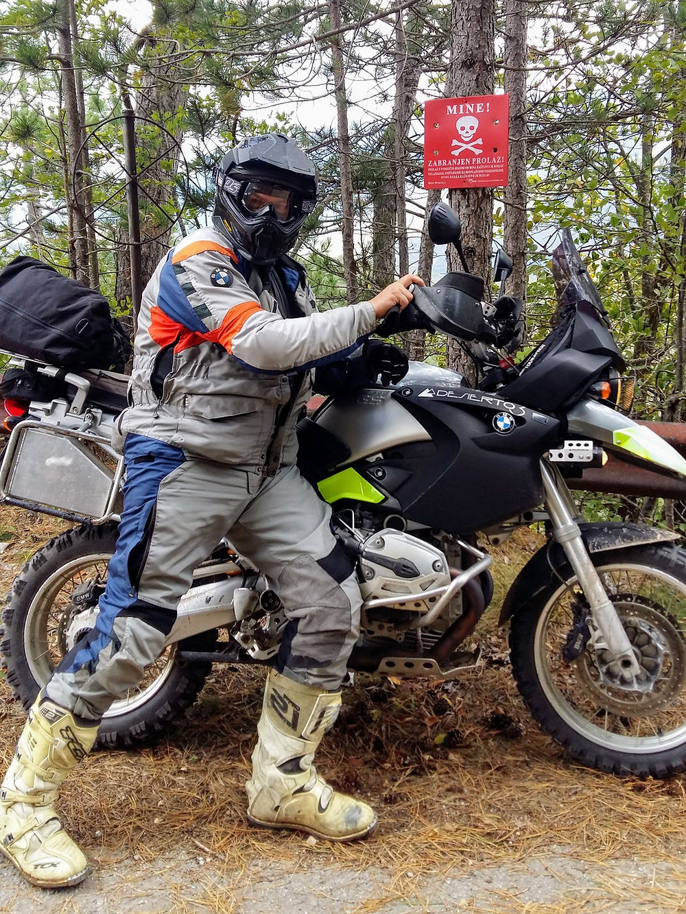 Motorkář na enduro motorce u cedule s lebkou v lese.