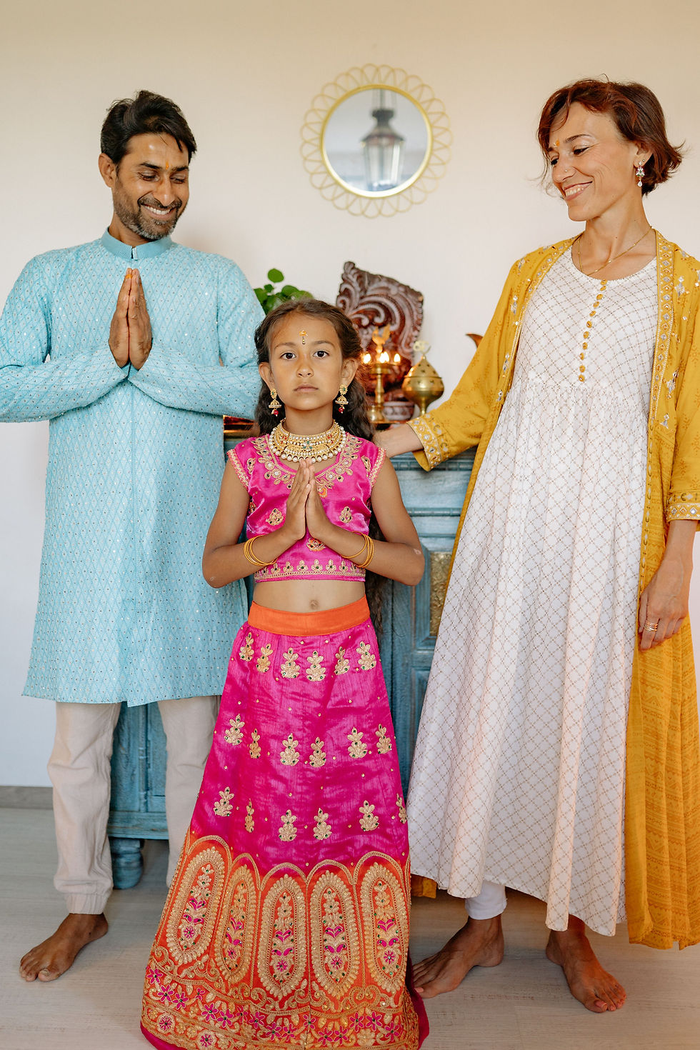 An intercultural deși couple în Indian outfit with their daughter doing namastey