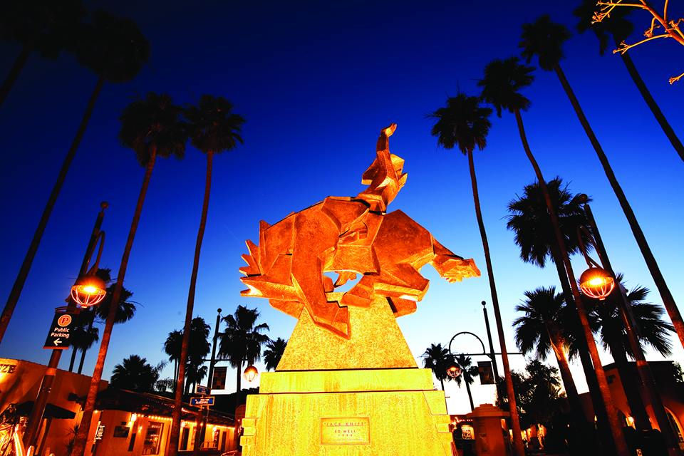 Bucking horse and rider statue in front of blue skies and palm trees